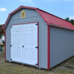 10x16 Lofted Gambrel Barn shed with gray siding, red trim, white double doors, a yellow gable vent, and red metal roofing.