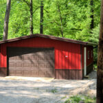 custom one-car garage with a brown door, red siding, brown foundation, and a brown roof on a stone driveway