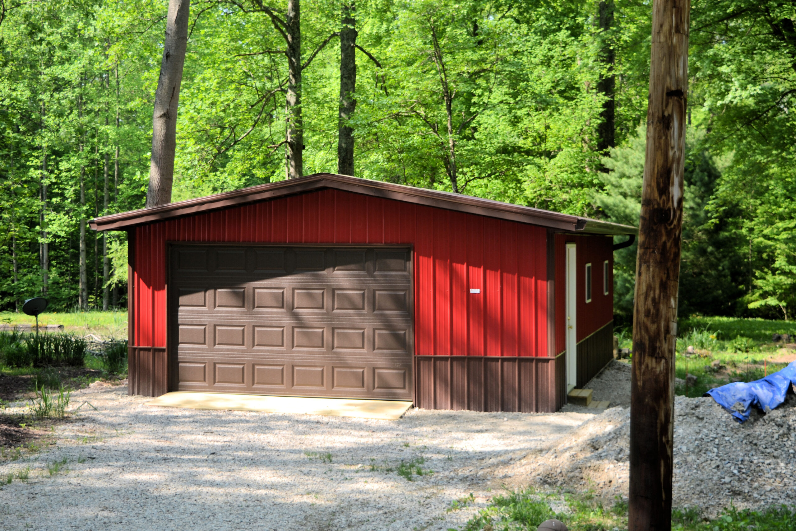 custom one-car garage with a brown door, red siding, brown foundation, and a brown roof on a stone driveway