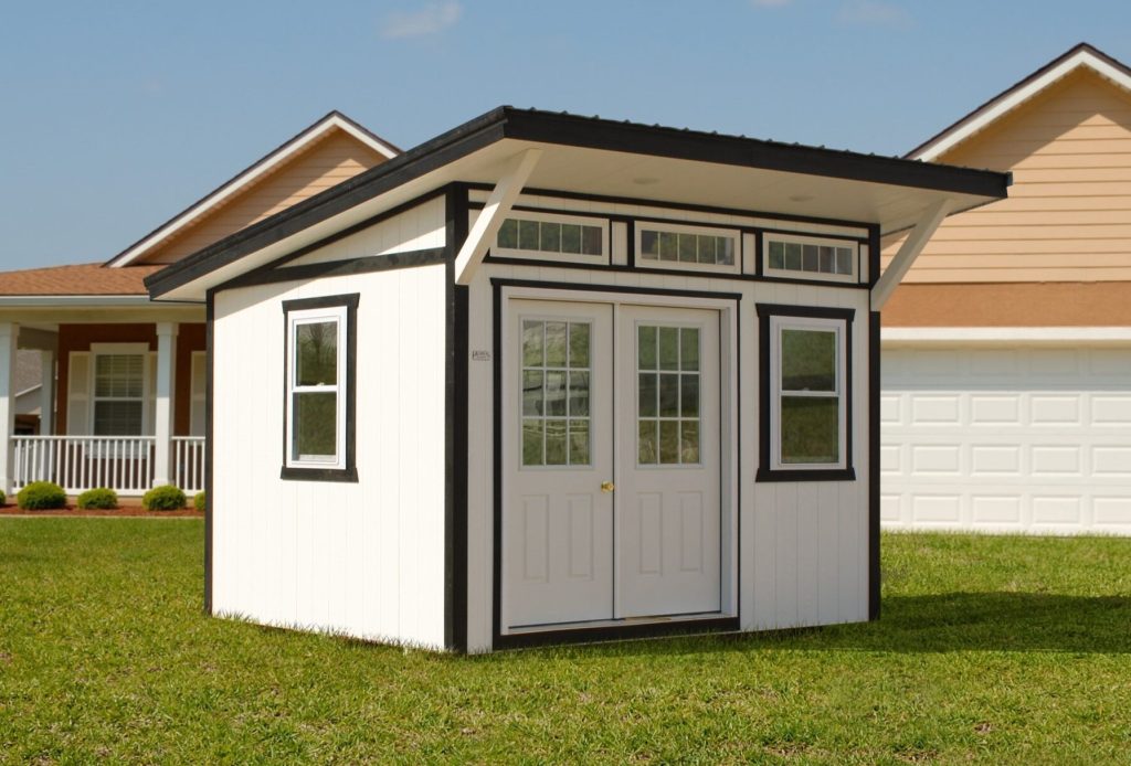 Studio shed with white siding, black trim, 3 transom windows, double doors with glass, and 2 windows.