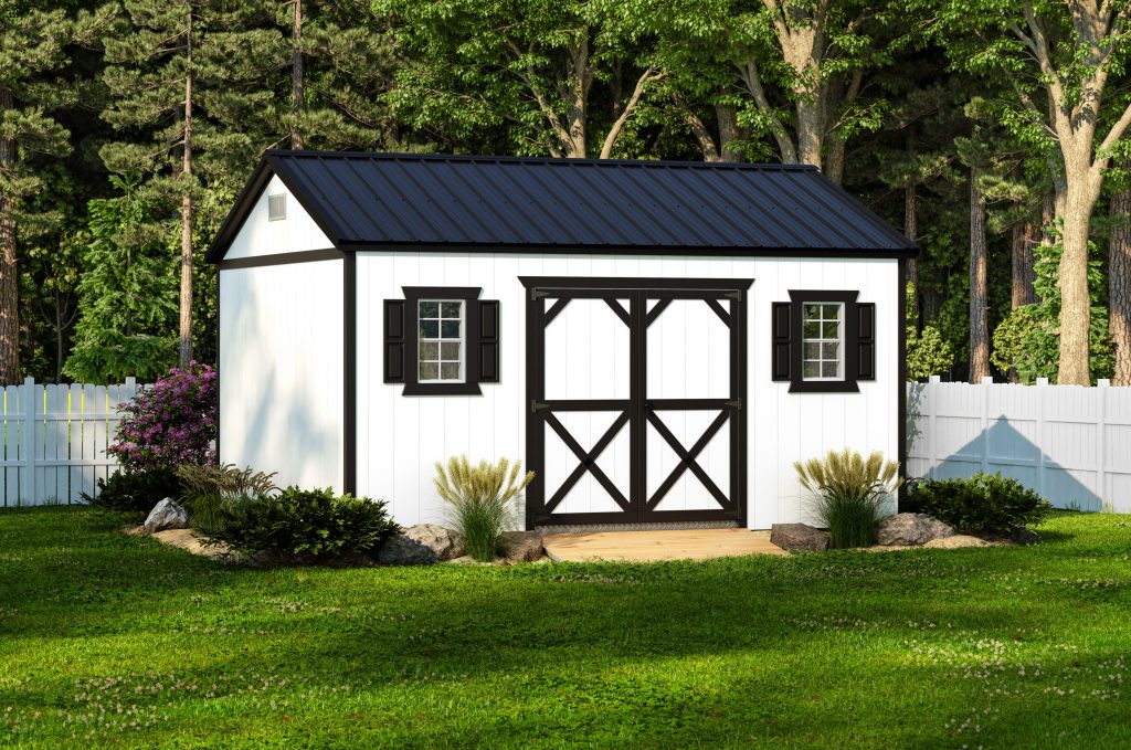 White shed with black trim, double doors, 2 windows with black shutters, and a black metal roof sitting in a backyard in front of a white fence.