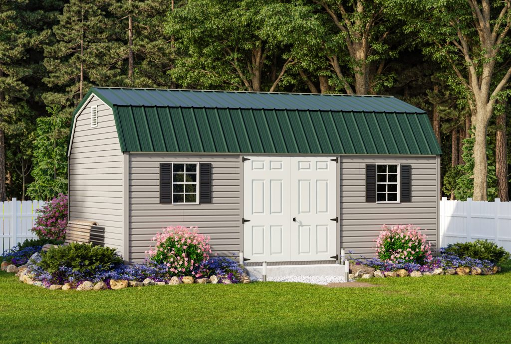 Lofted Garden Shed with light gray siding, white double doors, 2 windows with black shutters, and a green metal roof sitting in a backyard in front of a white fence.