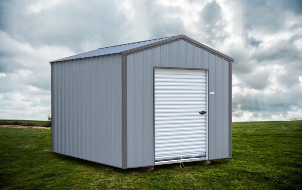 Metal shed with light gray siding, dark gray trim, and a white roll-up garage door.