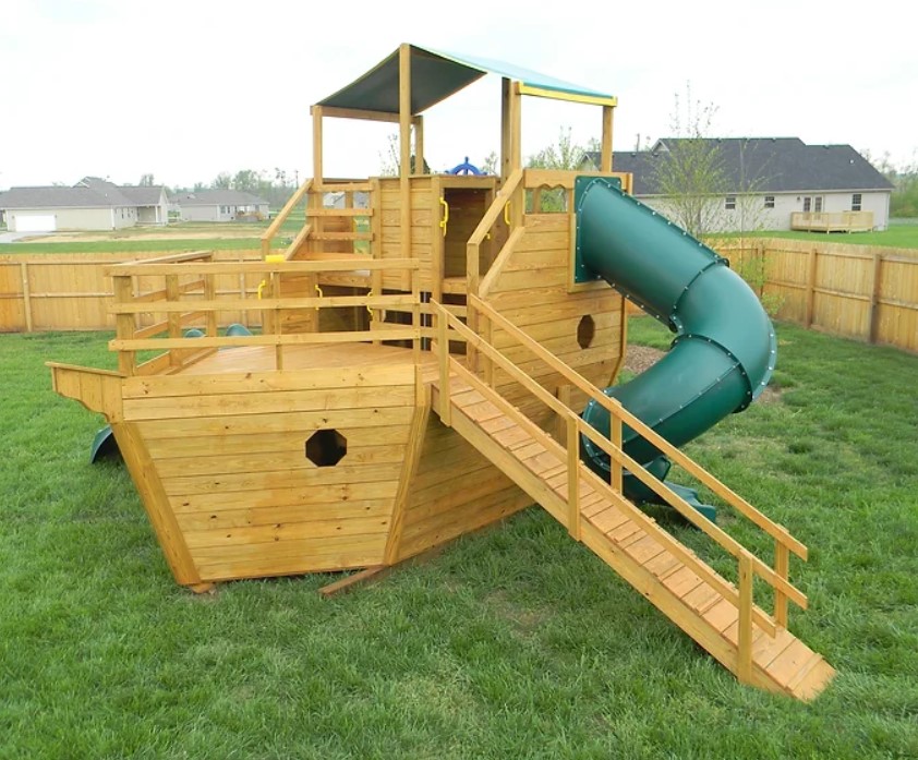 Wood pirate ship playground with a green tube slide.